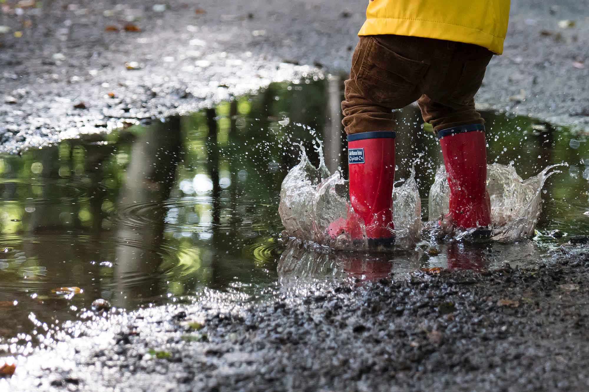 Bambino con stivali da pioggia rossi che sguazza in una pozzanghera.