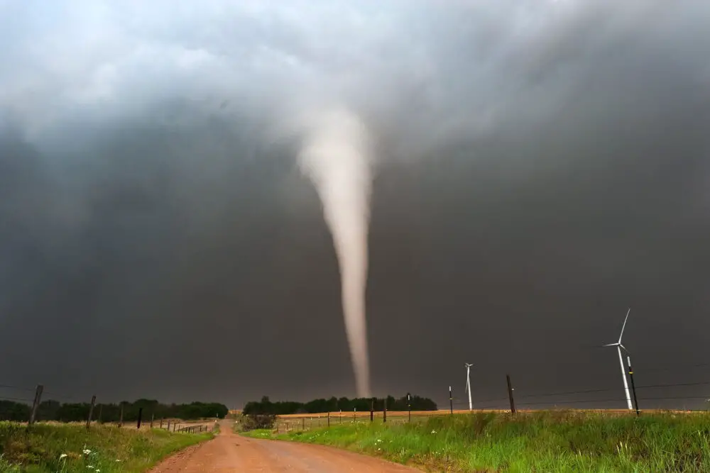 Ein Tornado bildet sich über einer ländlichen Landschaft mit Windkraftanlagen.