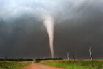 Tornado se formando em uma paisagem rural com turbinas eólicas.