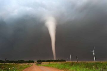 Tornado forming over rural landscape with wind turbines.