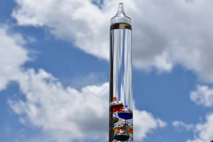 Galileo thermometer with blue sky and clouds in background.