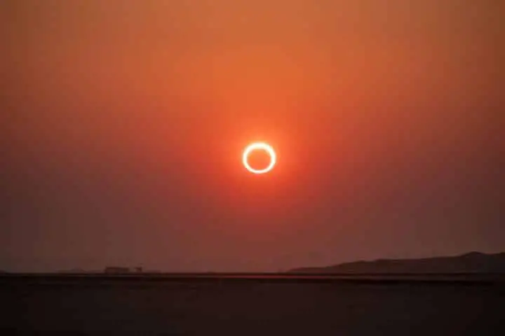 Sonnenfinsternis bei Sonnenuntergang über einer Silhouettenlandschaft.