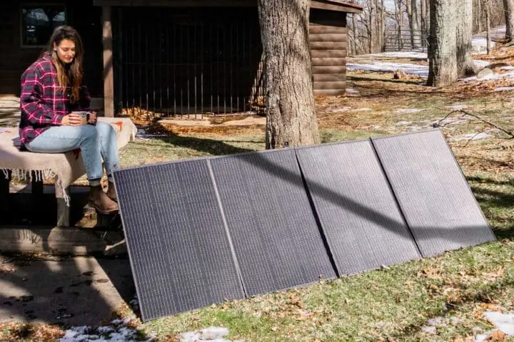 Vrouw met draagbare zonnepanelen in besneeuwd bos.